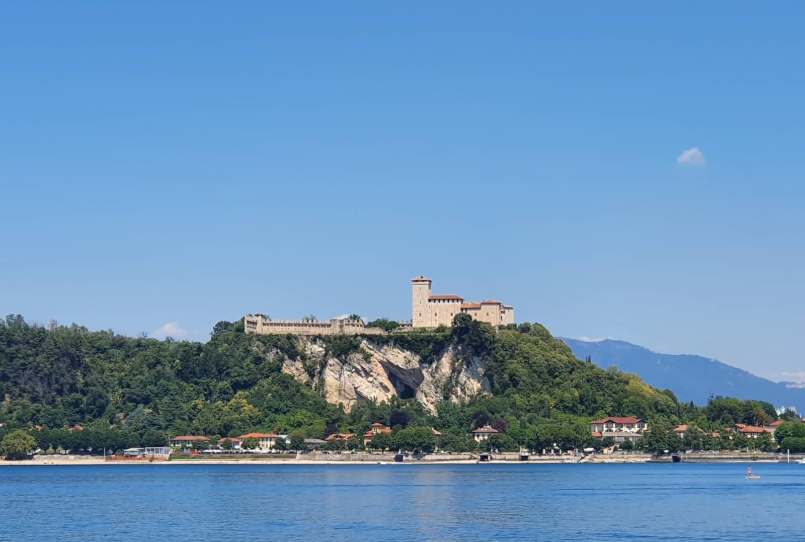 The Rocca d'Angera, a medieval fortress set on a wooded rocky spur, seen from the far shore of Lake Maggiore.