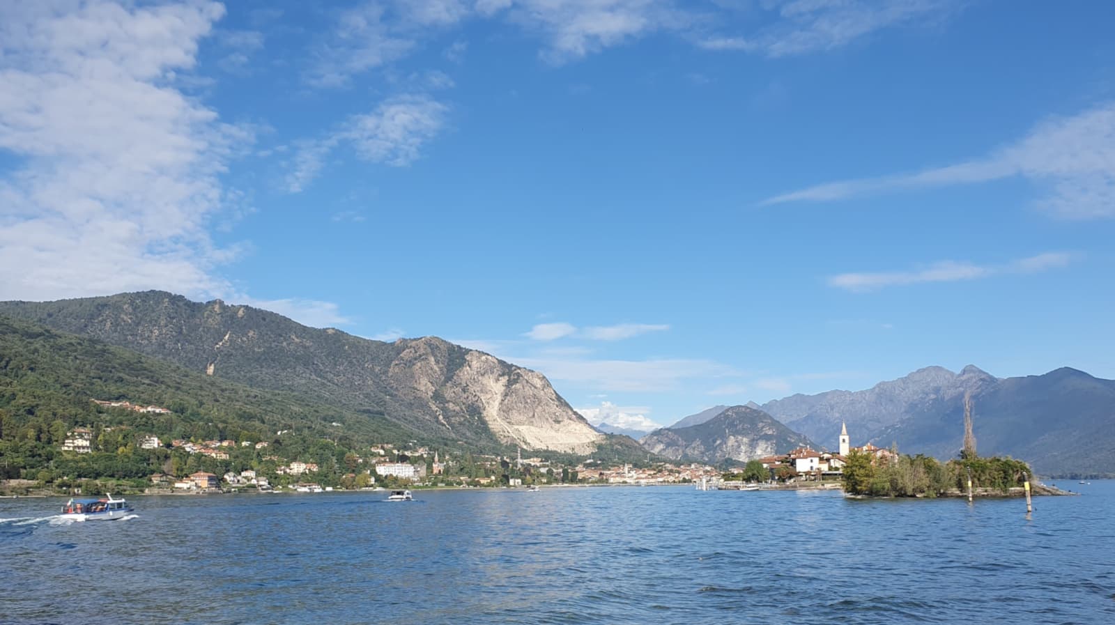 View over Lake Maggiore from Isola Bella: a small wooded island topped by a bell tower, with the mountains of the shore behind.